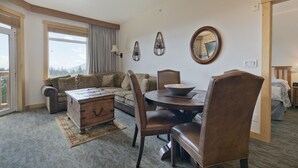 A hotel room with a dining area, a sofa, a wooden chest of drawers, and a large window with a view of mountains. - Ski-in / Ski-out 2Bed 2Bath Sunstone Lodge Condo at Little Eagle Express (Mammoth Lakes)
