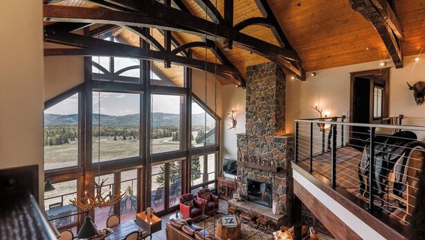 A spacious living area with a stone fireplace, large windows offering a view of the outdoors, and a wooden ceiling structure. - Amazing 3-level home.  Perfect for 3-generation family visits.  Sunsets & elk. (Angel Fire Resort)