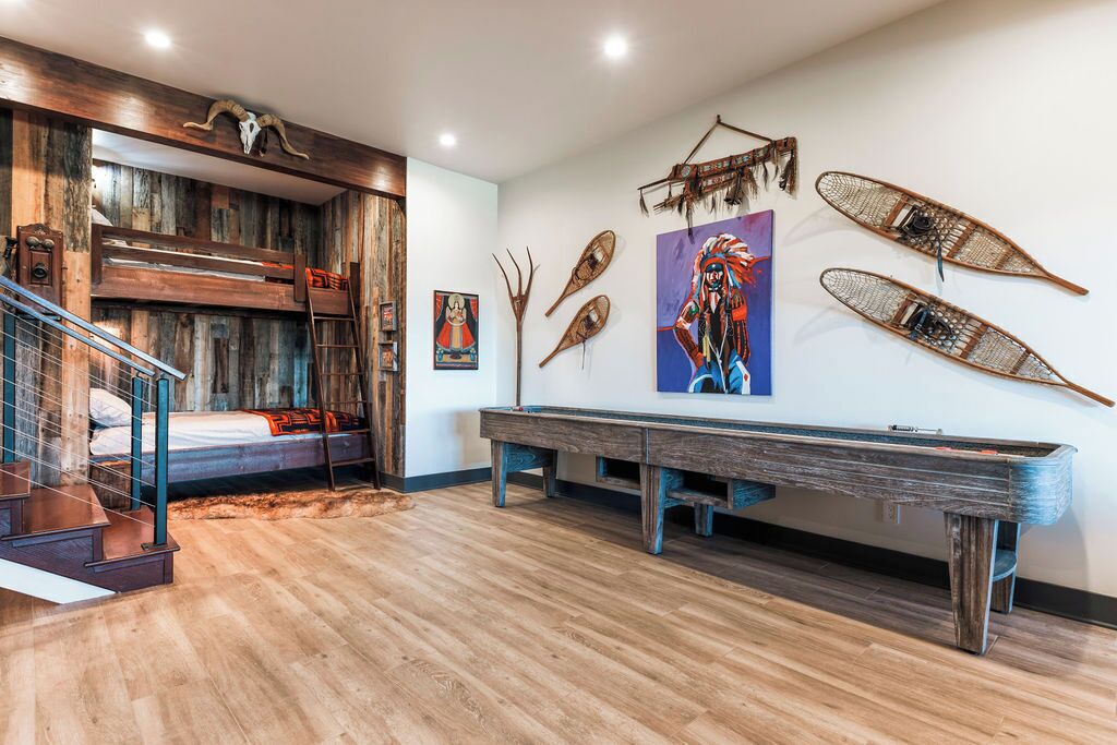 A room with a bunk bed, wooden flooring, a pool table, and wall art including a painting and decorative items.