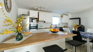 Una cucina moderna con mobili bianchi, un piano di lavoro in legno e un'area pranzo con tavolo e sedie.