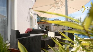 Patio esterno con mobili in vimini, piscina e parete in pietra.