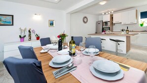 Un'area pranzo moderna con un tavolo di legno apparecchiato per quattro persone, circondato da sedie. Sullo sfondo, si intravede una cucina con mobili bianchi e un piano di lavoro.