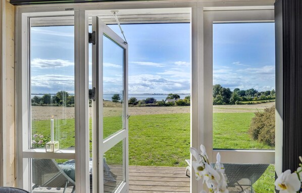 A room with a large glass door leading to a grassy outdoor area with a view of the sea.