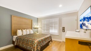 A bedroom with a bed, bedside lamps, a window with blinds, a television, and a wooden cabinet. - Hotel 414 Anaheim, Luxurious King Size Bed (Anaheim)