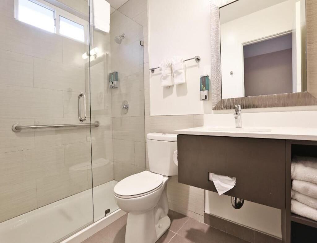 Et moderne badeværelse med brusekabine i glas, toilet, vask med håndklædestang og spejl.