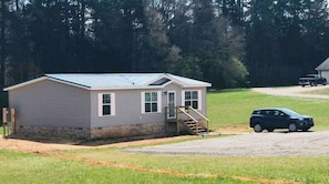 A single-story mobile home with a metal roof, a front porch, and a driveway.