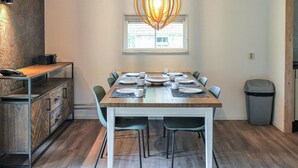 Un coin repas avec une table en bois dressée pour six personnes, entourée de chaises vertes, d’un mur à motifs et d’un luminaire suspendu.