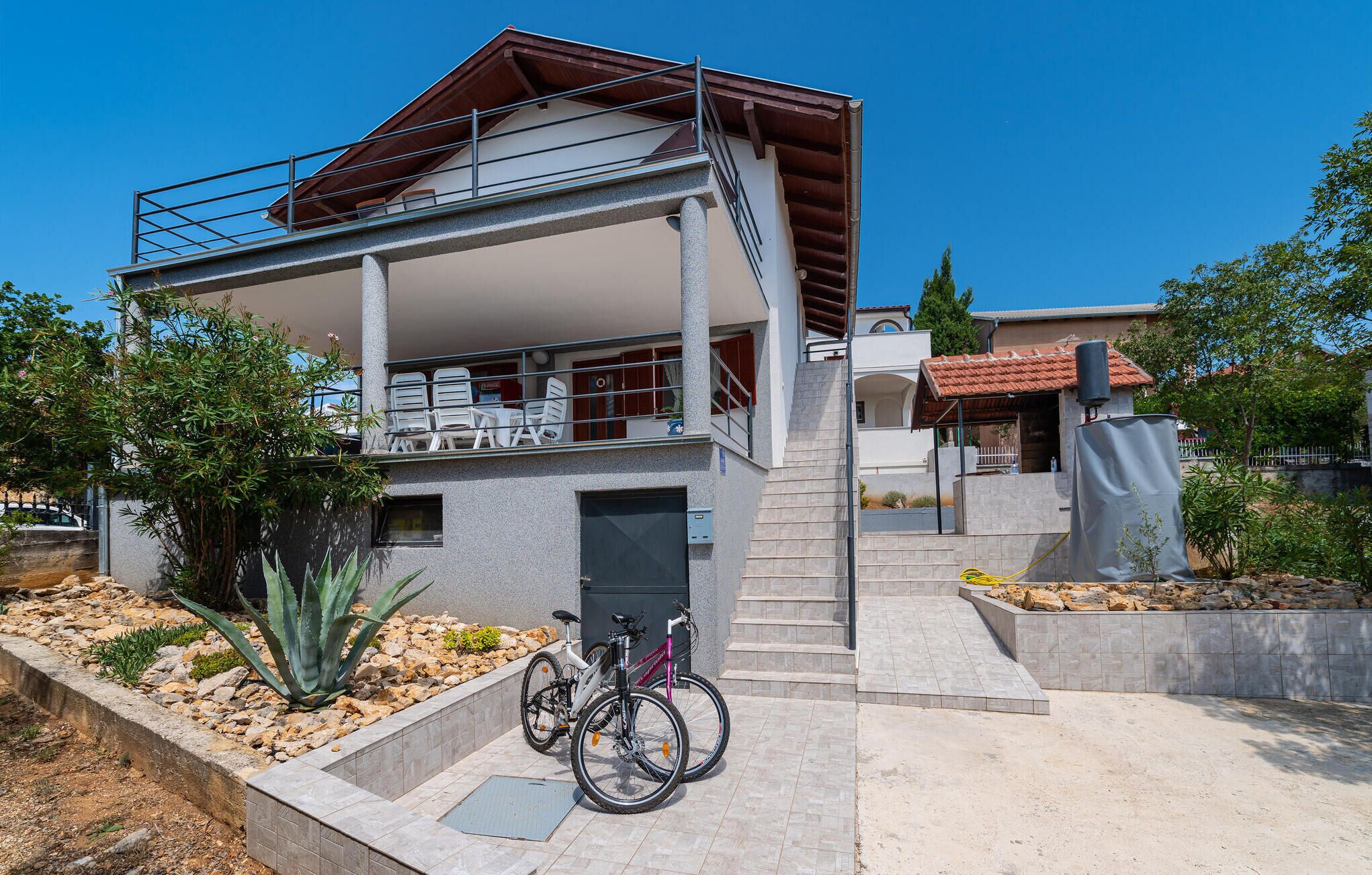 Un immeuble de deux étages doté d’un balcon, d’un escalier et d’un vélo garé devant.