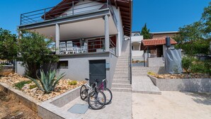 A two-story building with a balcony, a staircase, and a bicycle parked in front. - Beach front apartment in Maslenica (Maslenica)