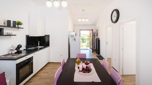 A modern kitchen with white cabinets, a black countertop, and a dining area with a table set for two. - Beach front apartment in Maslenica (Maslenica)