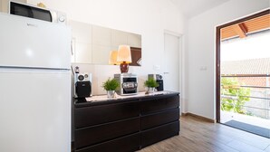 A modern kitchen with a white refrigerator, a black countertop, a microwave, a coffee machine, and a small potted plant. - Beach front apartment in Maslenica (Maslenica)