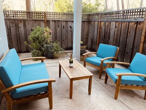 A patio area with wooden furniture, including a sofa and two chairs, a small table with a bottle and glasses, and a wooden fence in the background. - Wine country retreat within walking distance of restaurants, wineries and more (St. Helena)