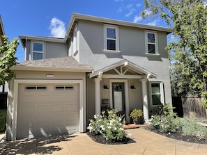 A two-story house with a garage, a front porch with columns, and a well-maintained garden with white flowering plants. - Wine country retreat within walking distance of restaurants, wineries and more (St. Helena)