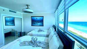 Habitación de hotel con dos camas, ventilador de techo, obras de arte y vista a la playa.