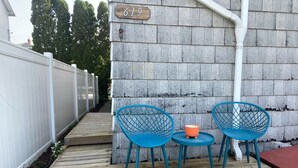 Eine Holzterrasse mit zwei blauen Stühlen und einem kleinen Tisch, einem weißen Zaun sowie der Hausnummer 619.