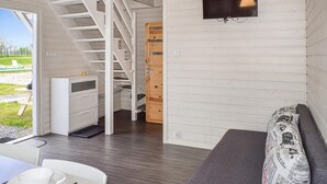 Un intérieur moderne avec un escalier, un téléviseur fixé au mur, un canapé et un coin repas comprenant une table et des chaises.