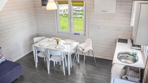 Une cuisine compacte comprenant un coin repas, des meubles blancs, un évier et une fenêtre donnant sur l’extérieur.