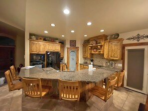 Kitchen features a large island with a countertop, wooden chairs, and a sink, oven, and refrigerator.