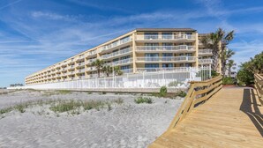 A beachfront hotel with multiple balconies, a wooden boardwalk, and a sandy beach.