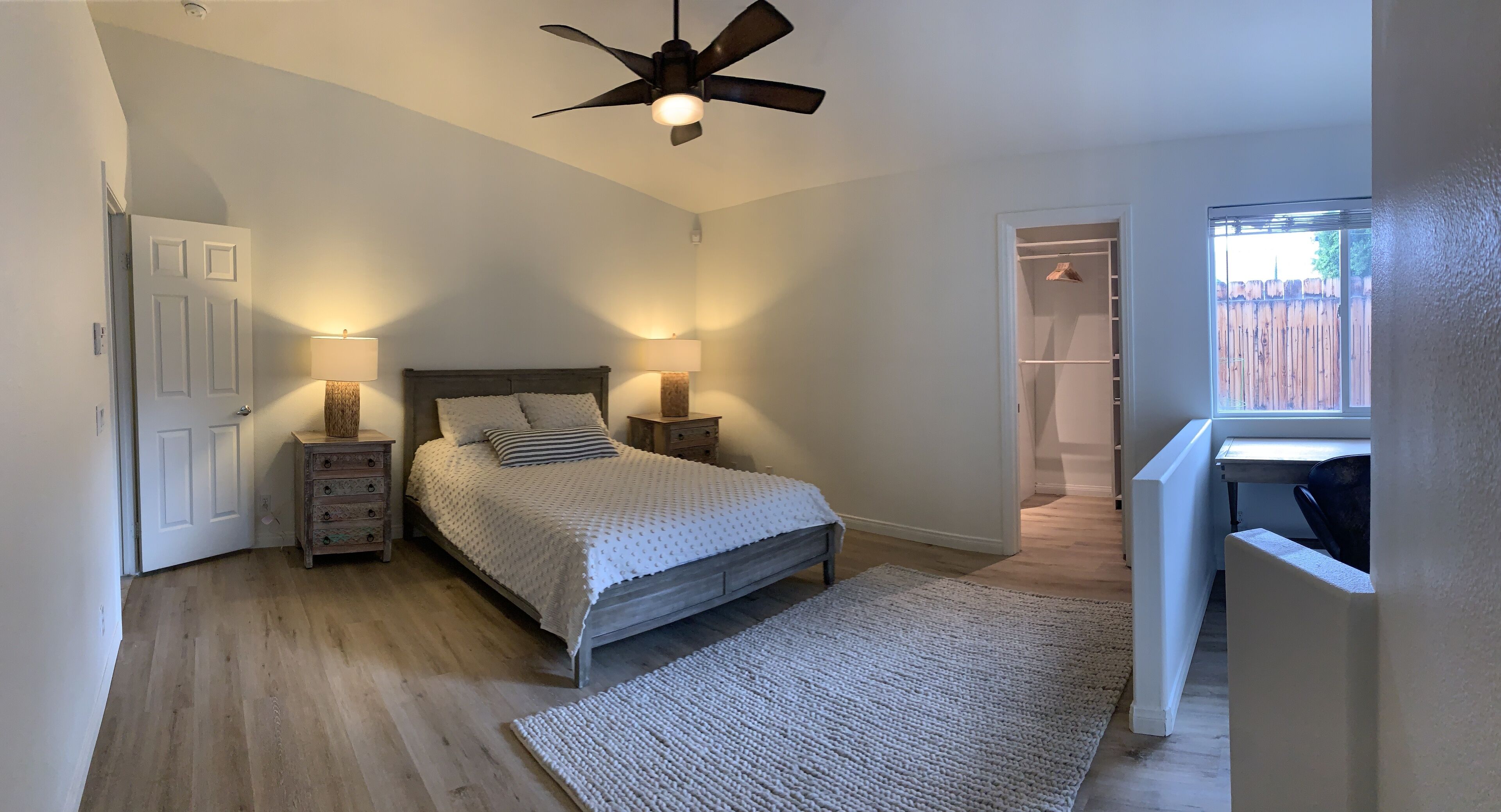 Une chambre à coucher comprenant un lit, des lampes de chevet, un ventilateur de plafond, une commode en bois, un tapis et un placard avec vue sur le jardin arrière.