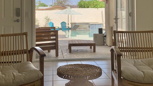 Ein Terrassenbereich mit Pool, Holzstühlen, einem Tisch und einem Sonnenschirm.