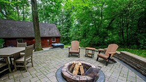 Eine Terrass mit Feuerstelle, Holzstühlen und einem Tisch.