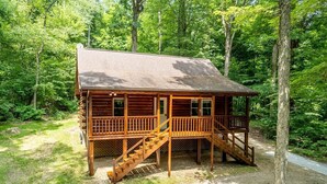 Eine Holzhütte mit Veranda und Treppe, umgeben von dichtem Wald.