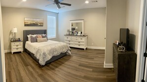 Une chambre à coucher comprenant un lit, des tables de chevet, une commode, un téléviseur et un ventilateur de plafond.