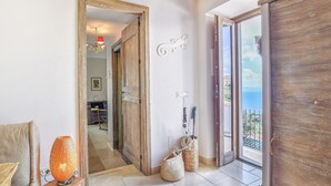 Ein Flur mit Holztür, Blick auf das Meer und einem kleinen Tisch mit Lampe.