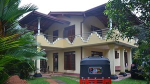 A two-story building with a balcony, a red auto-rickshaw parked in front, and a well-maintained lawn. - Villa Vinses In Hikkaduwa (Hikkaduwa)