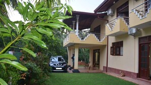 A two-story building with a covered porch, a car parked in front, and a dog sitting on the ground. - Villa Vinses In Hikkaduwa (Hikkaduwa)