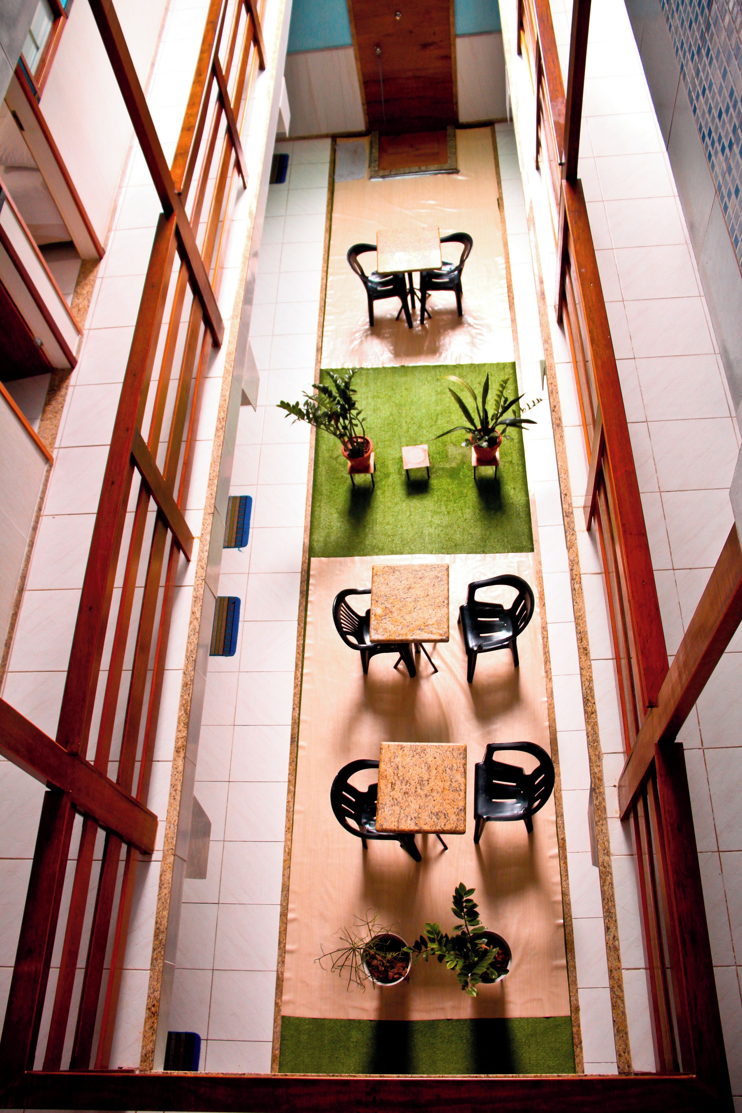 A corridor with a central seating area featuring tables and chairs, potted plants, and a tiled floor.