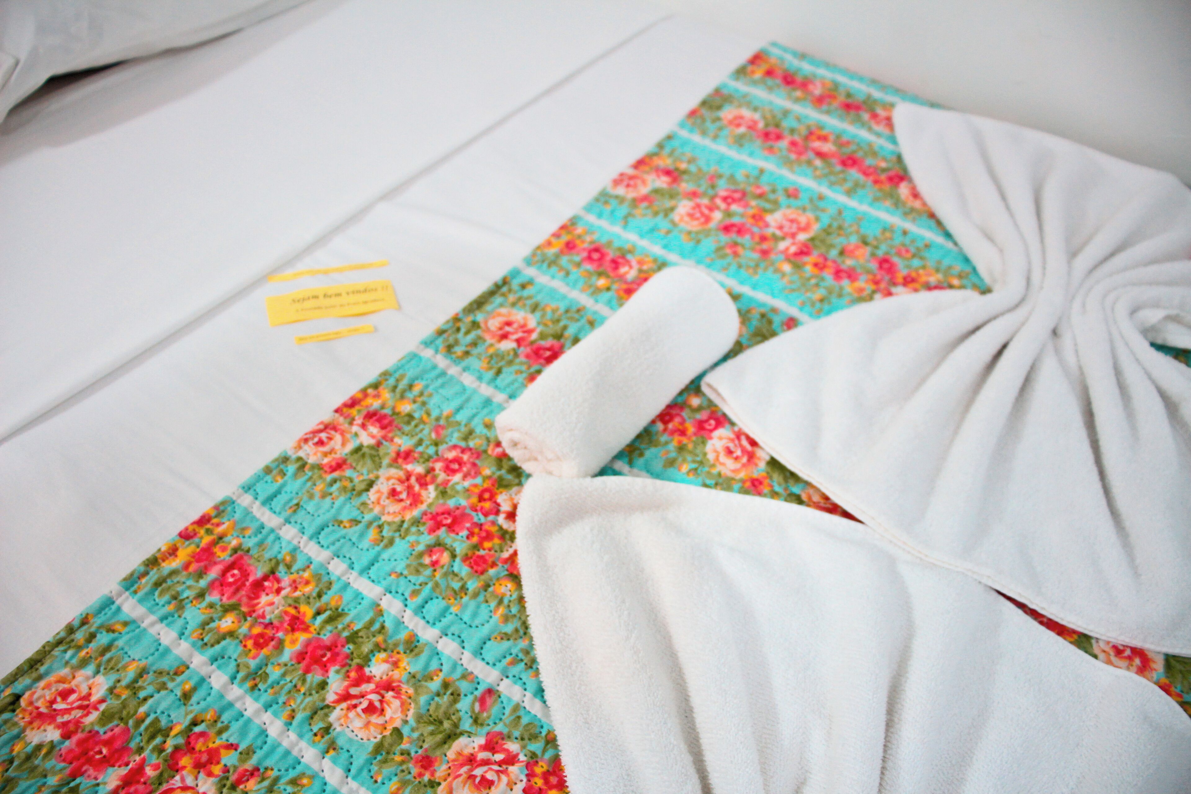 Una toalla blanca doblada con cuidado y una alfombra de baño con estampado floral sobre una superficie blanca.