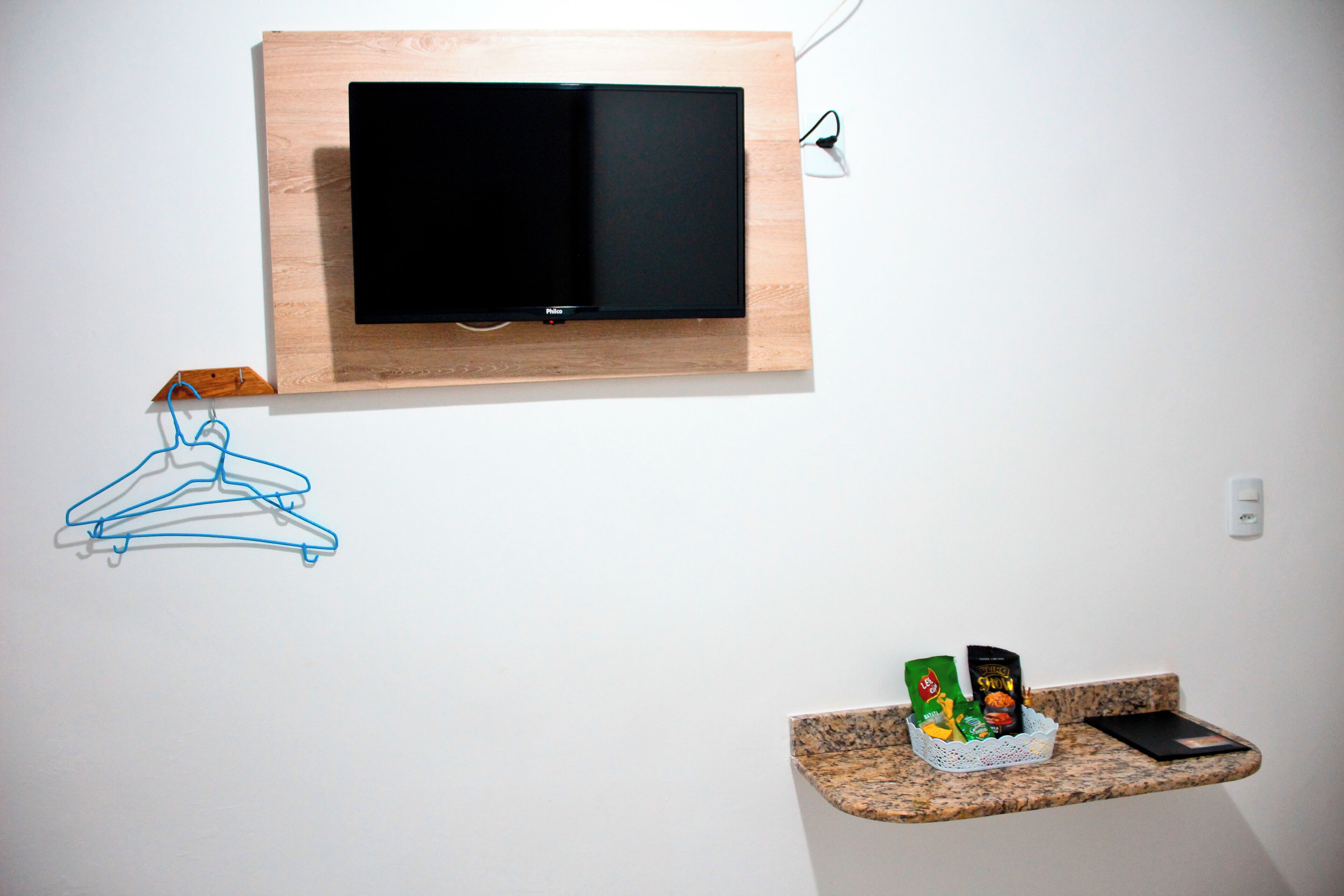 A wall-mounted TV, a clothes rack, a basket with snacks, and a smartphone on a granite countertop.