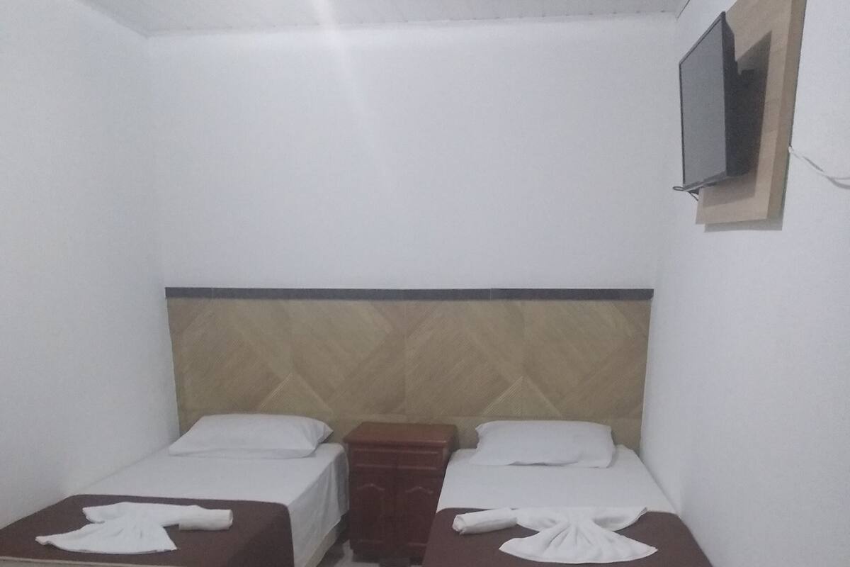 A small, clean room with two beds, a wooden headboard, a small wooden nightstand, and a TV mounted on the wall.