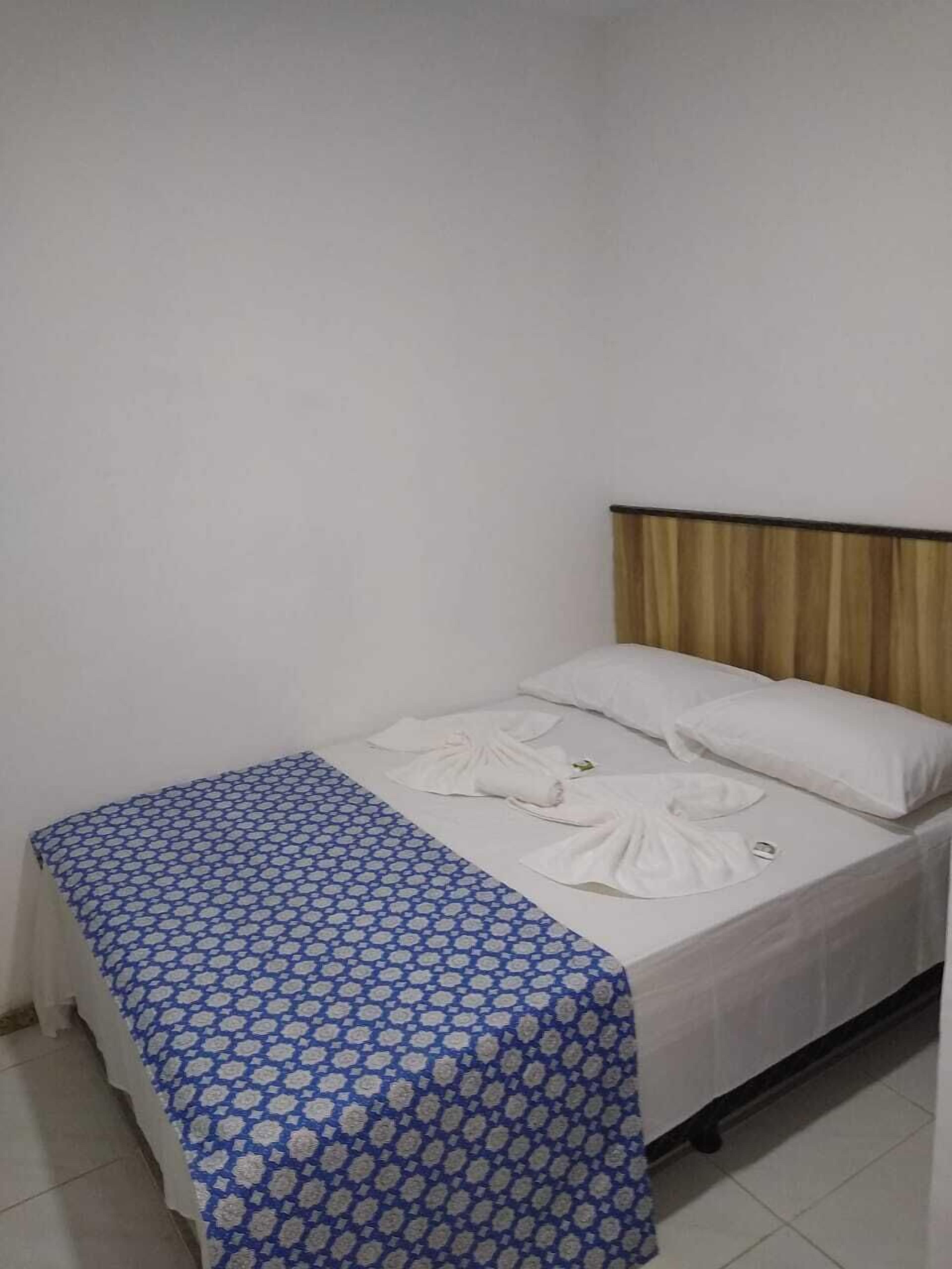 Un lit simple avec une couvre-lit bleue et blanche à motifs, des oreillers blancs et une tête de lit agrémentée d’un rideau.