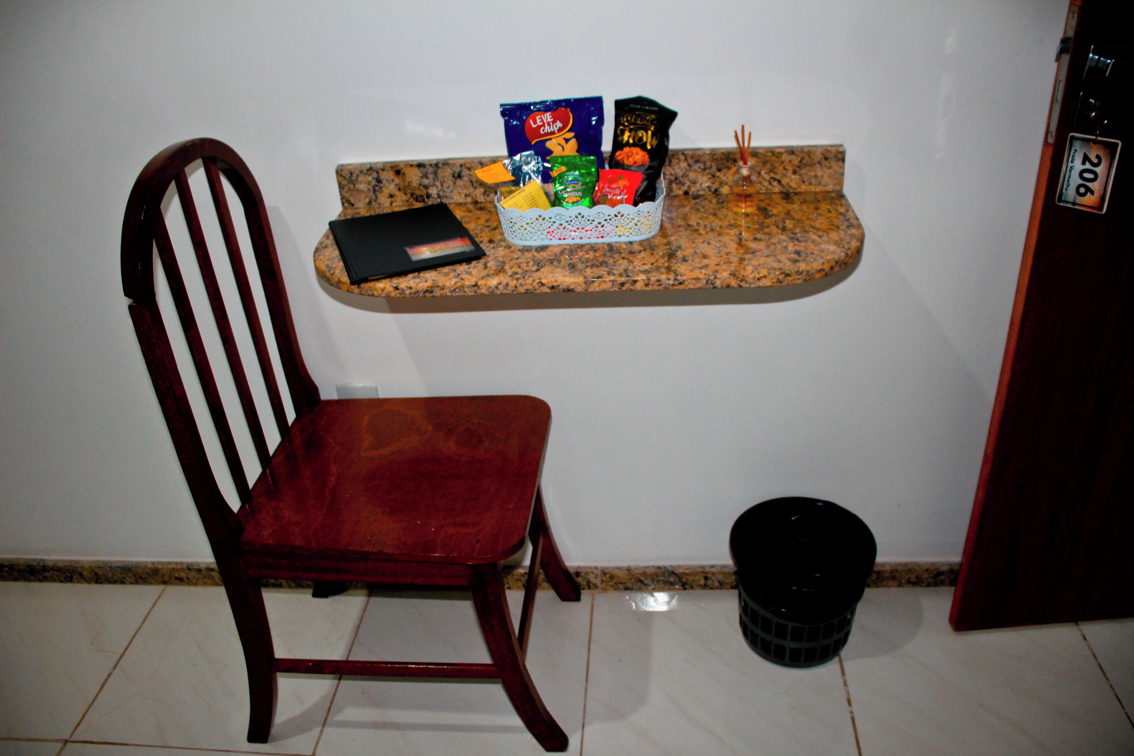 Une chaise en bois, un petit panier contenant des collations, une poubelle noire et une porte avec une plaque numérotée.