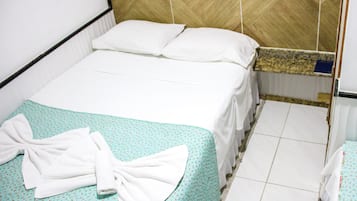 Een netjes opgemaakt bed met een deken met groene en witte patronen, twee kussens en een witte handdoek die erover is gevouwen.
