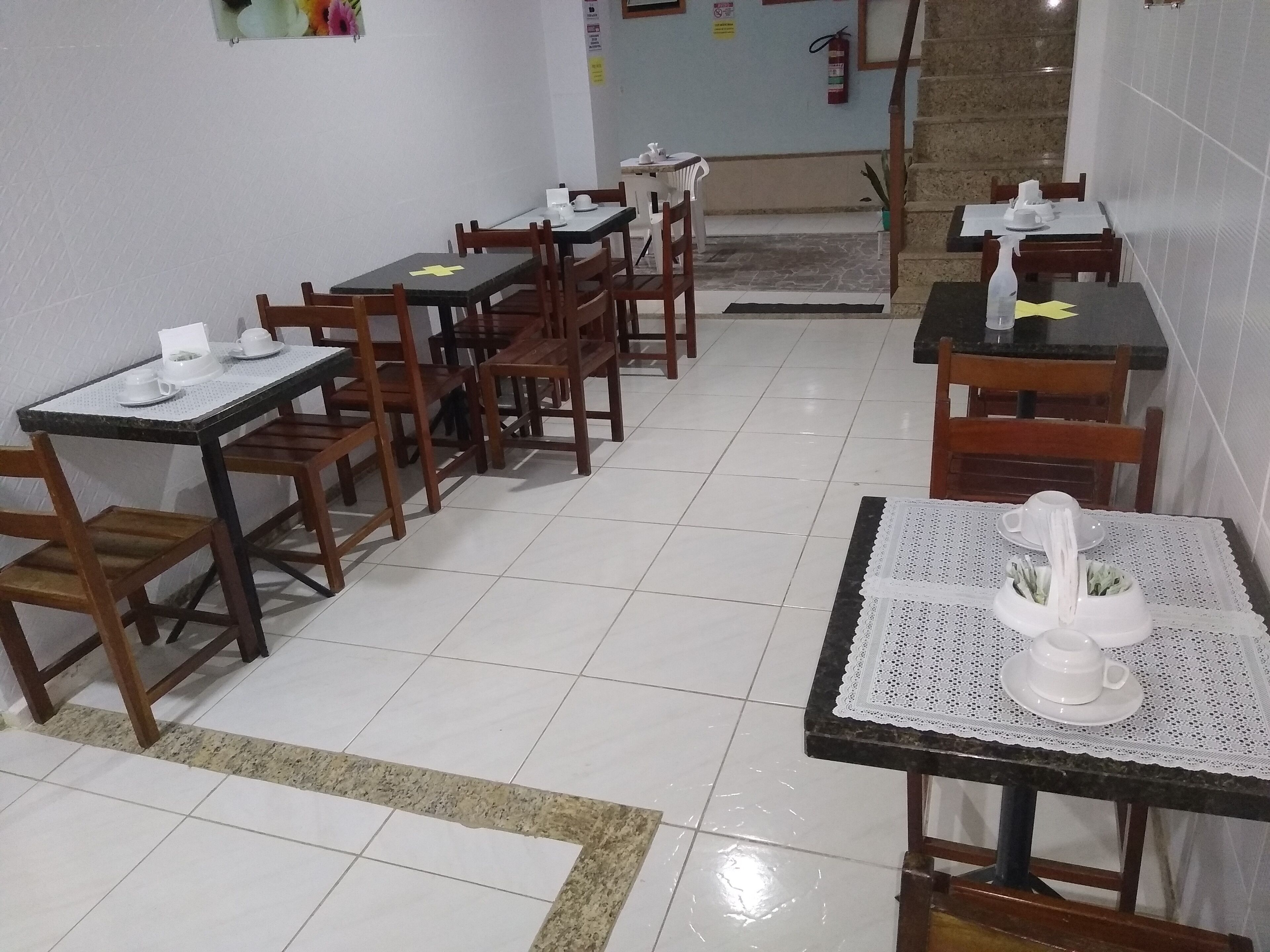 Un espace repas avec plusieurs tables et chaises, un extincteur accroché au mur et un escalier en arrière-plan.