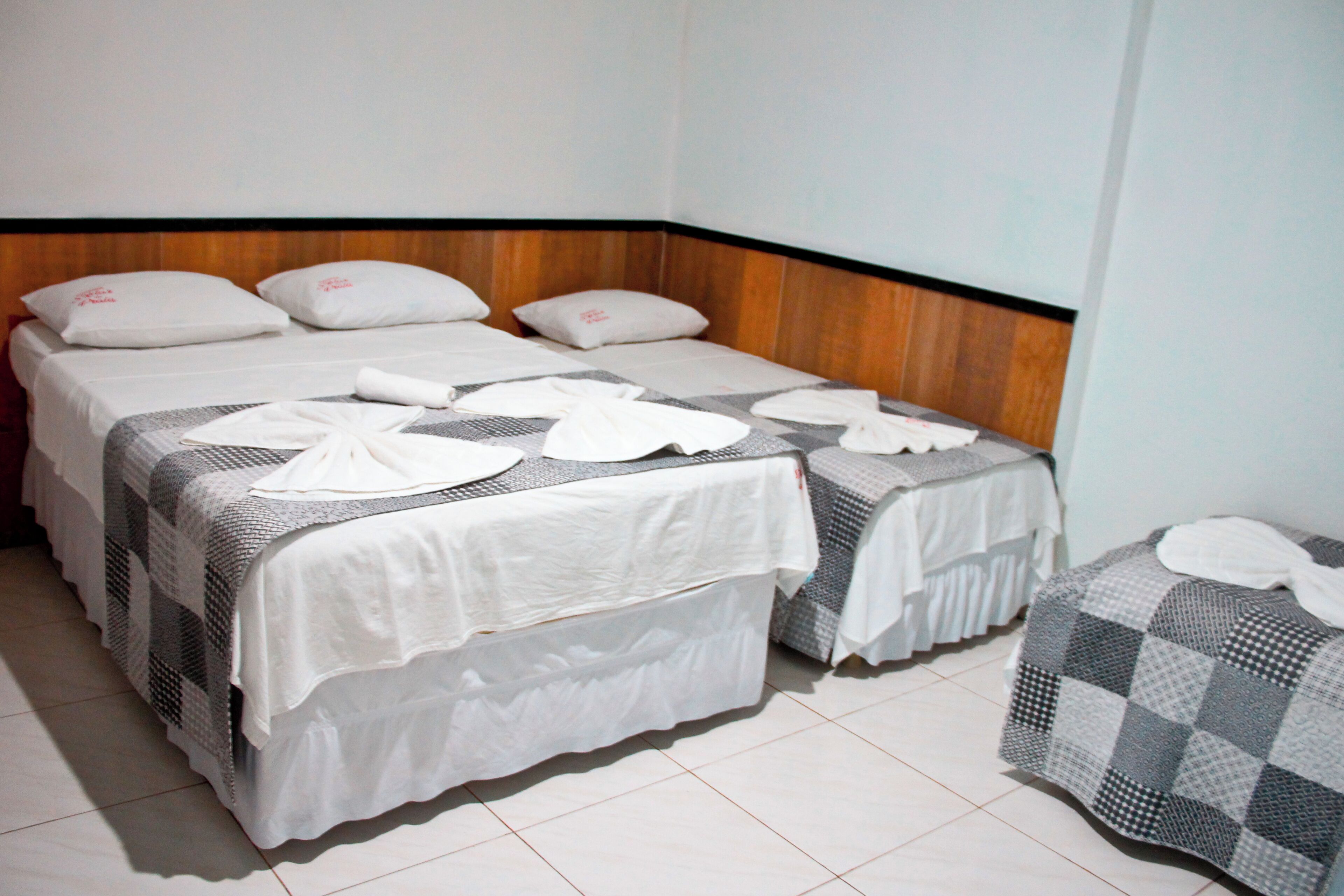 Une chambre d’hôtel avec deux lits, chacun recouvert d’une courtepointe blanche et agrémenté d’oreillers, et une courtepointe à carreaux sur le côté.