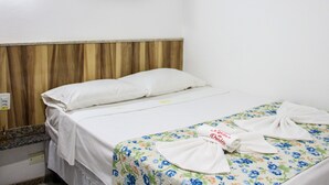 Une chambre d’hôtel avec un lit, une tête de lit en bois, un téléviseur fixé au mur qui diffuse une scène de plage et une couvre-lit à motifs floraux.