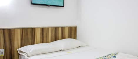 A hotel room with a bed, a wooden headboard, a wall-mounted TV displaying a beach scene, and a floral bedspread.