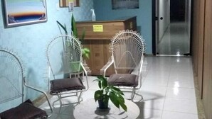 Un espace d’accueil avec un mur bleu, un comptoir de réception et une enseigne sur laquelle on peut lire « FOUSADA ». On y trouve deux chaises blanches en fil de fer et une petite table ronde avec une plante.