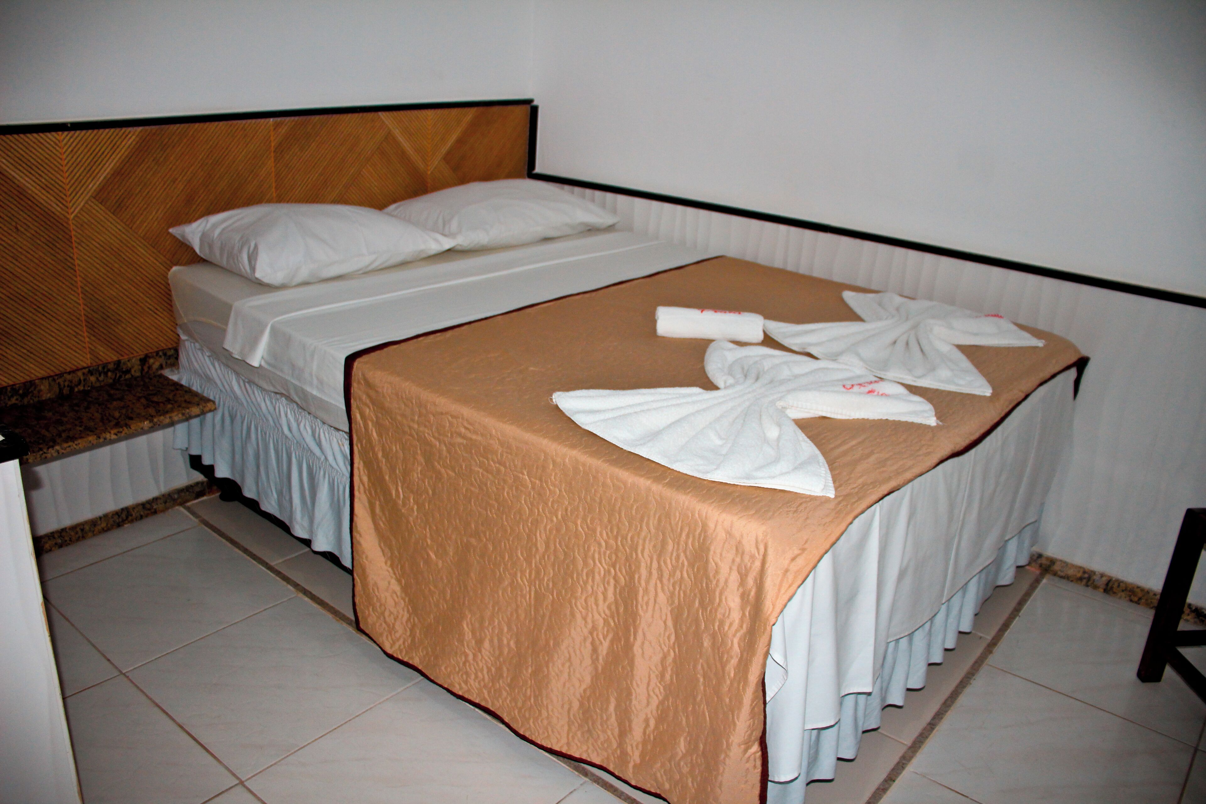 A neatly made bed with a brown bedspread and white linens, a wooden headboard, and a small bedside table with a mirror.