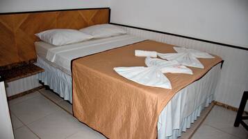 A neatly made bed with a brown bedspread and white linens, a wooden headboard, and a small bedside table with a mirror.