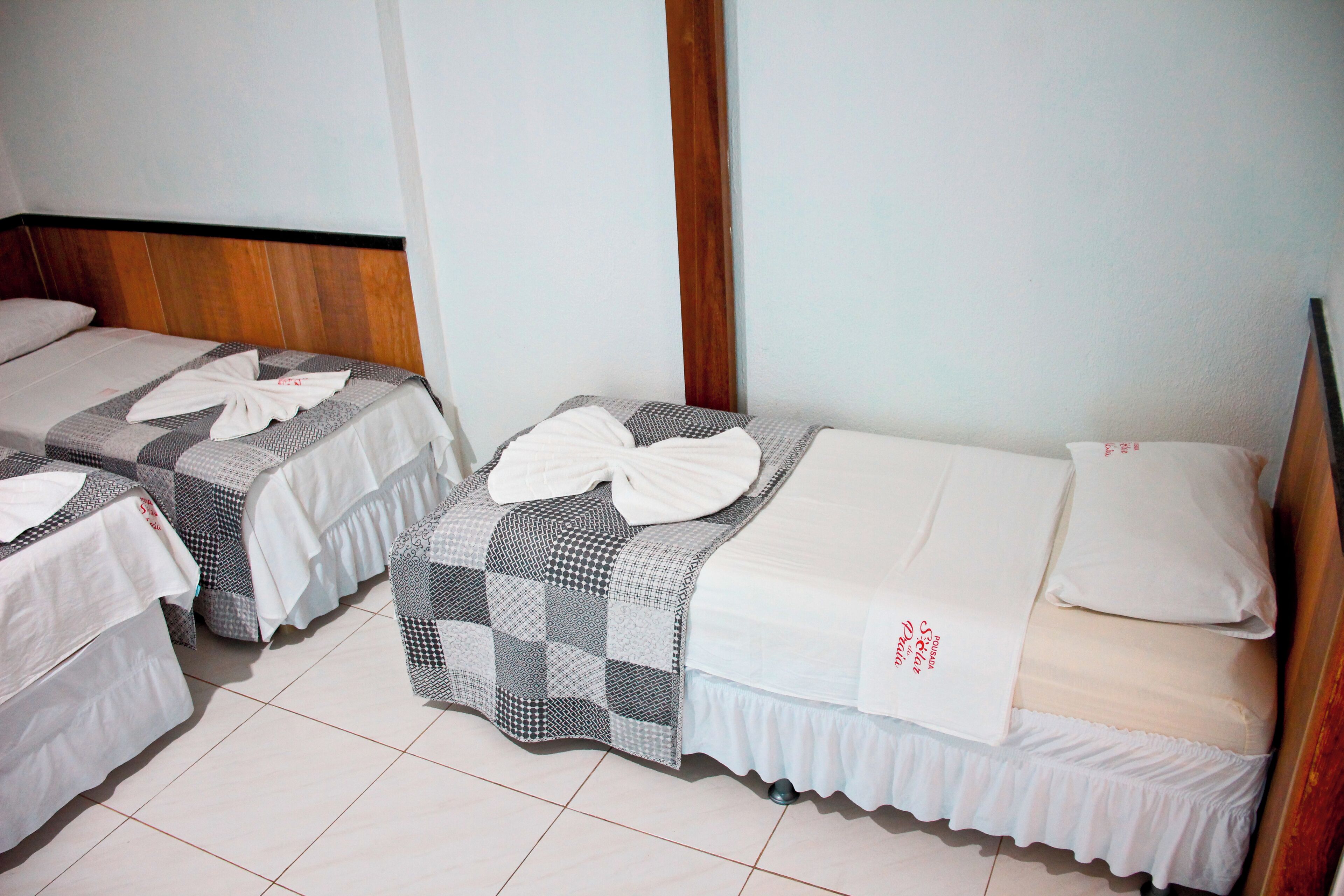 Una habitación de hotel con dos camas individuales, cada una con una colcha blanca y almohadas ordenadas.