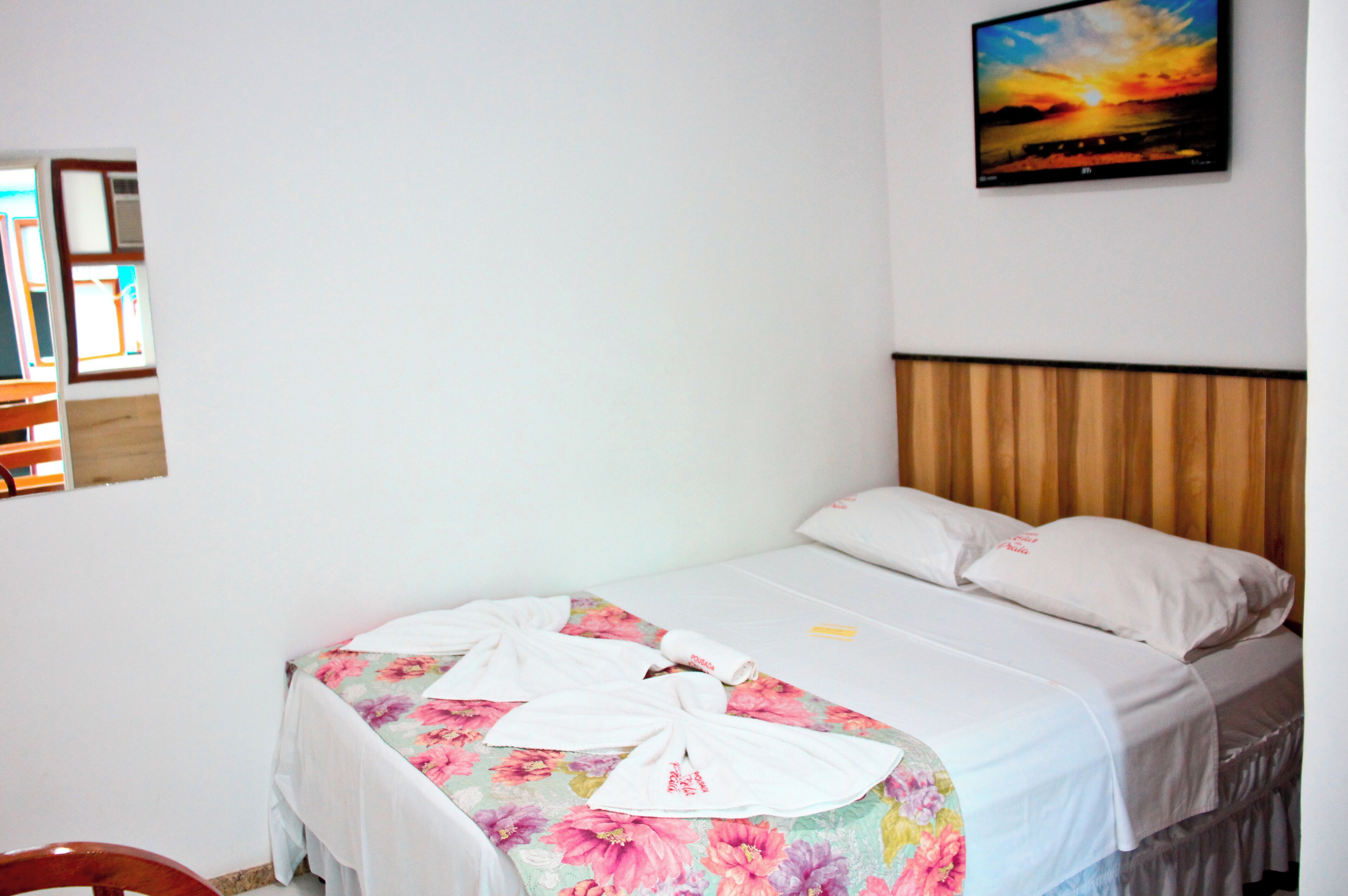 Una cama bien hecha con una colcha floral, un cabecero de madera y un cuadro de un atardecer en la pared.