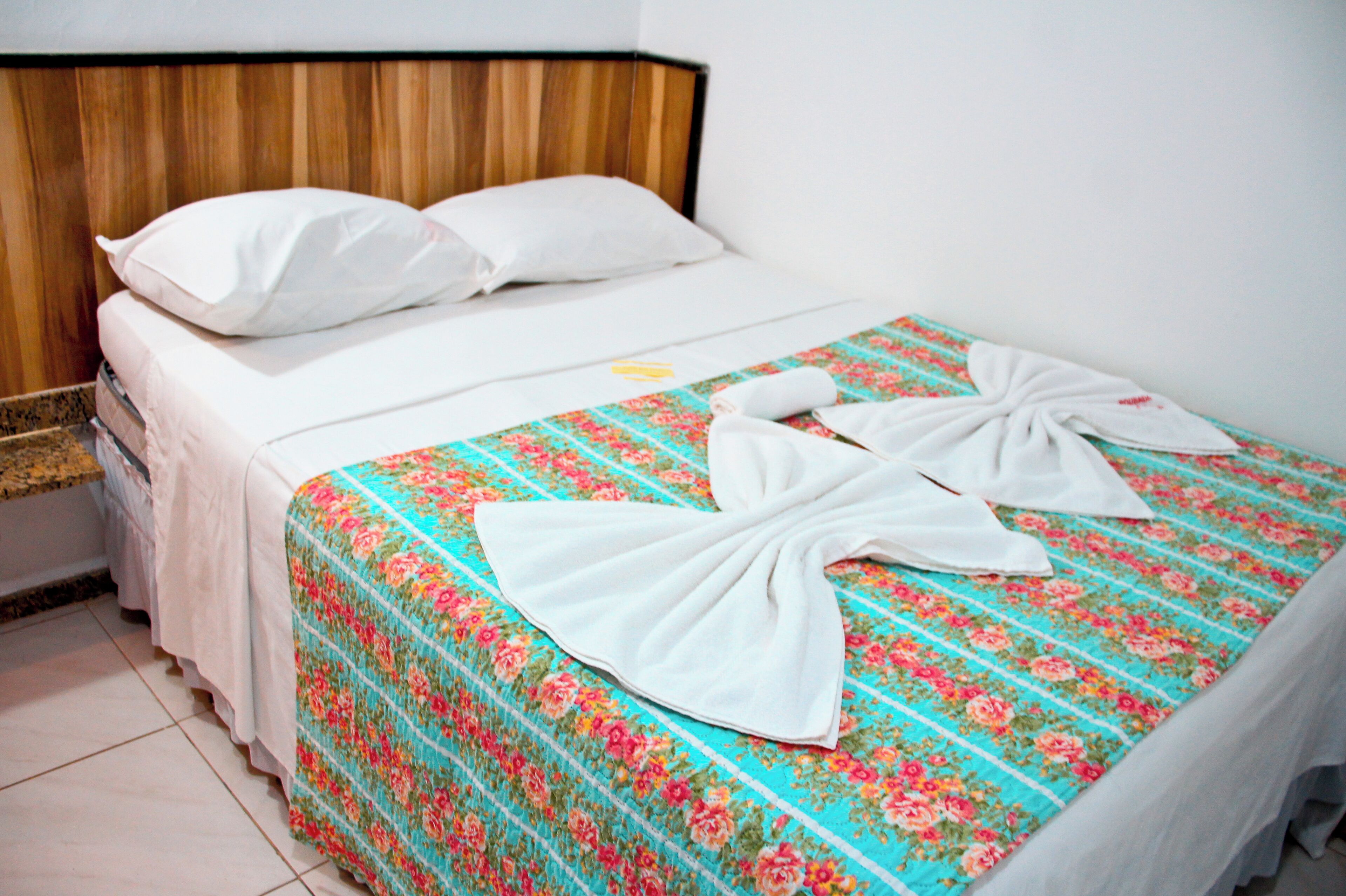 A neatly made bed with a floral bedspread and two towels arranged in a bow shape.