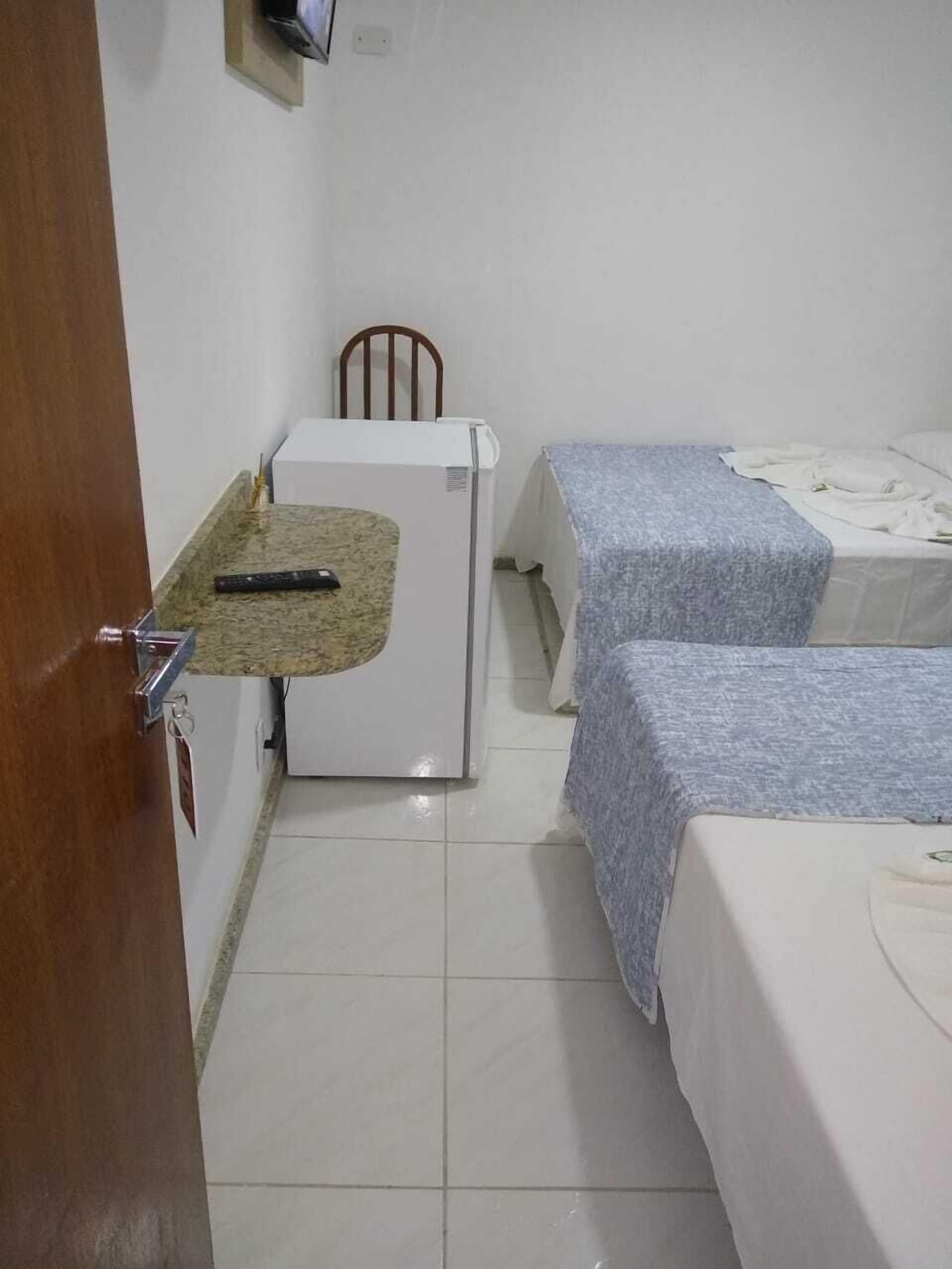 A small, clean room with a kitchenette, two single beds, and a wooden chair.