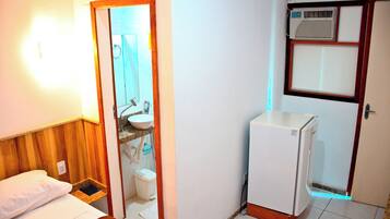 A compact hotel room with a bed, a small bathroom with a sink and toilet, and a white refrigerator.